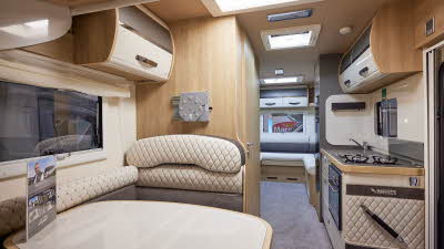 Mobilvetta Tekno Line K-Yacht 95 has two tone grey and cream embossed upholstery.  There are two tone overhead lockers. The floor has a grey carpet.  Towards the rear of the vehicle there is a rear lounge.