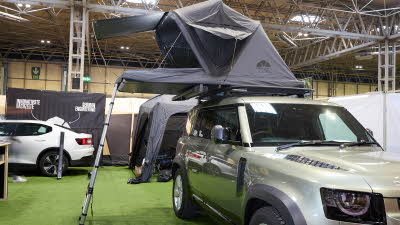 The Roof Space 4 is fully extended on a Land Rover Defender.  The canvas is pale grey, with a black porch.  There is a platform with a sturdy ladder to gain easy access.
