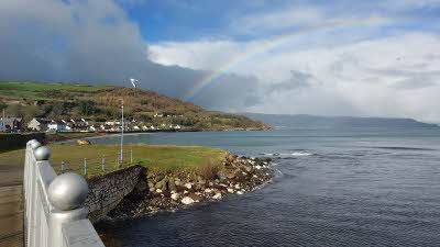 Rainbow seen over the bay at Glenarm, County Antrim. An iron railing is seen in the foreground