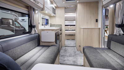 Interior of the Elddis Avanté APEX 550 with dark grey sofas, wood accents and grey carpets.  The large roof light will let natural light flood in.  The rear bedroom door is open.