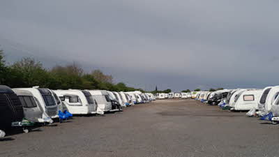 Caravans lined up on tarmac with tress behind and a greyish sky