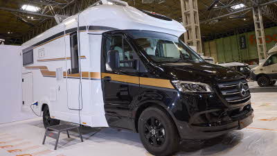 The Malibu Mercedes-Benz T 450 RB-LE lightweight 3.5t has a black cab with a white body and gold decals.  There is a black step by the habitation door.  The two skylights are open.
