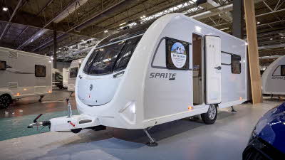 Swift Sprite Alpine 4 DB is white with black decals.  Its corner steadies are down and its entrance door is open.