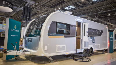 Buccaneer Starliner Cruiser has a grey exterior with a black decal with a teal and yellow strip under the window.  The entrance door is open and there is a black metal step to gain easy access to the interior.