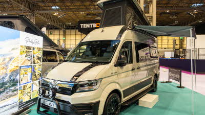 The Knights Custom Conversions Prestige XL is cream with black decals.  Its pop top is open and it has a green awning.  It has a cream step to gain easy access.