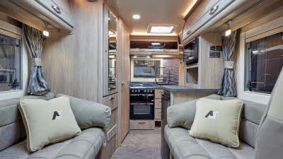 Auto-Sleeper Nuevo EK has two toned grey embossed upholstery, with light wood overhead cabinets.  A full sized oven, fridge and microwave is in the end kitchen.  There are patterned curtains in the windows.