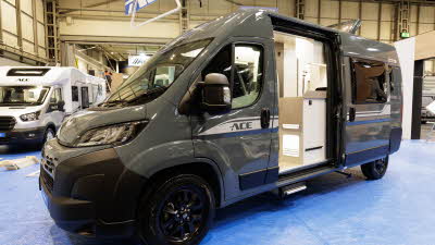 The Ace Motorhomes 1200 RL is grey with white decals, its sliding door is open as is its rear roof light