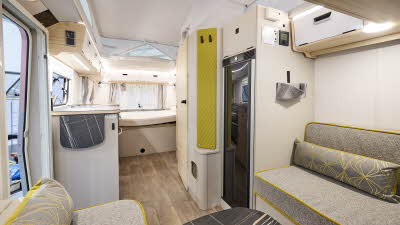 Interior of the Eriba Touring 630 Urban with grey sofas, lime green accents and a wooden floor.  To the rear there is a large fixed bed.
