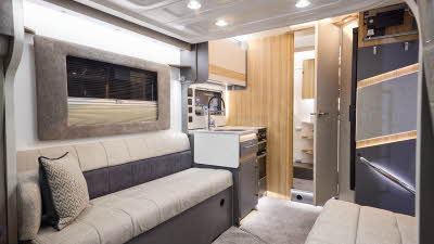 The Bailey Adamo 60-2 has grey carpets, with cream and pale wood cabinets. The upholstery is cream and dark brown. There is a step to the rear washroom. There is a mid brown plinth around the lounge window.