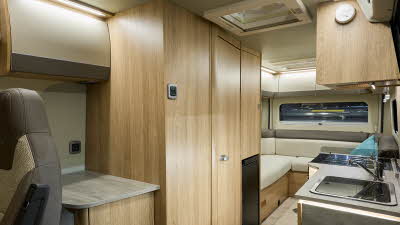 Auto-Trail V-Line 635 Sport's interior has beige upholstery with a turquoise cushion.  The furniture is wooden and it has two skylights.  There is a rear lounge with the kitchen hob and sink are to the right.