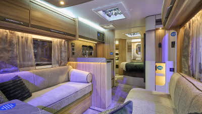 Bailey Alicanto Grande Deluxe Evora’s interior has beige upholstery with wooden furniture.  There is a fixed island bed to the rear of the caravan with mirrors.  There are two roof lights.