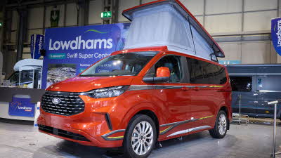 The Swift Monza is orange, its pop top roof is open and the canvas is pale blue.