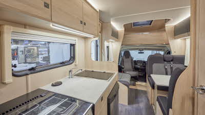 Auto-Trail Expedition C72 has two tone upholstery, with pale wooden furniture.  A hob, with a fridge underneath and a separate oven is in the kitchen.  The floor is dark wood.