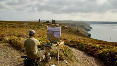 a man paints at an easel near the cliffs on the North Cornwall coast