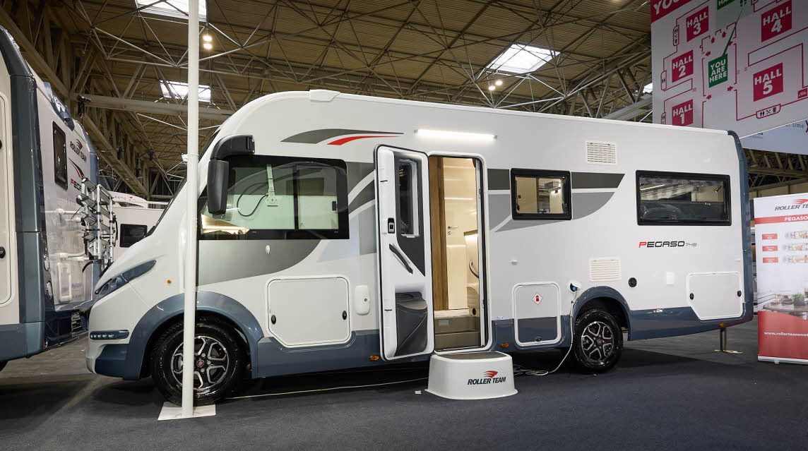 Roller Team Pegaso 745’s exterior has a white body with blue bumpers.  It has grey and red decals.  The habitation door is open and there is a large white step to gain easy access.