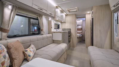 Elddis Avanté 868’s interior has beige upholstery with pale wooden furniture.  The kitchen is in the middle and the bedroom door is open revealing a French transverse fixed bed.