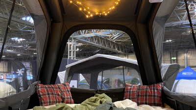 The interior of the Dometic TRT 140 Air has a bed with a cream rug, a green sleeping bag, two Tartan style cushions and overhead fairy lights