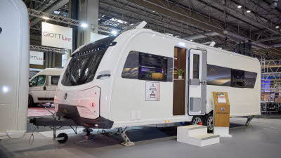 The Coachman LUSSO II has a white exterior with a brown patterned decal.  Its sunroof is open.  The entrance door is open and there are two wooden steps to gain easy access.  There is a stand next to the steps.