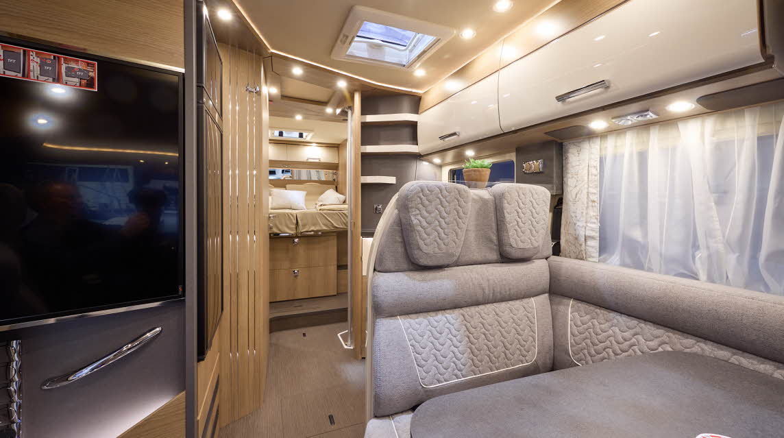 The Carthago C2-tourer I 148 RB-QB has a wooden floor, with cream cabinets.  The upholstery is grey  with white stitching.  There is a step up to the rear fixed bed.