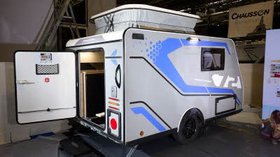 Trigano Mini Freestyle 300 Sport Edition's exterior is grey with blue decals. Its entrance door is open and there is a black step to gain access.  Its pop top roof is open.