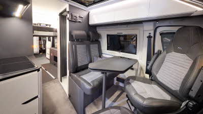 The Adria Twin Supreme’s floor has a pale brown carpet, with white cabinets and dark grey panels.  There is a large panoramic sunroof.  The upholstery is two tone with dark edging.  There is a grey table which can be rotated.  