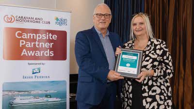 A Caravan and Motorhome Overseas Campsites Award Runner Up with the Chairman next to a sign showing Campsite Partner Awards, with Irish Ferries below it