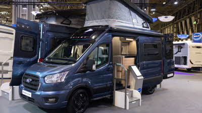 The Bailey Endeavour B65 is blue, its rising roof is extended.  The sliding door is open and there is a step to enable easy access.  The rear doors are open.