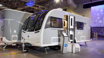 The Bailey Phoenix Black 440 has a grey exterior and a brown decal with light ripples on it.  The entrance door is open and there are two metal steps to gain easy access to the interior.  Next to the steps is an interactive stand.