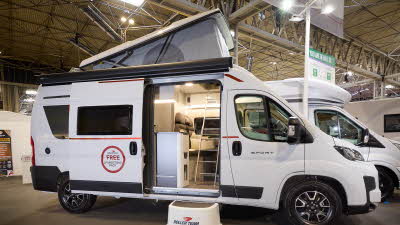 The Roller Team Livingstone 2 has a white exterior with black trim.  There is a white step outside the open sliding door revealing the interior.  The pop top roof is fully extended.