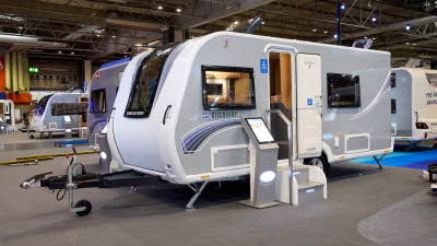 Bailey Discovery D4-4’s exterior has grey sides with a blue and white patterned decals. The front is white.   The entrance door is open and there are two metal steps to gain easy access.  There is an interactive display board to the left