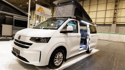 The Volksleisure Volkswagen Avoriaz T7 is white.  Its rising roof and sliding door are open.