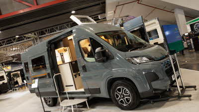 The Rimor Horus 54 is grey, its skylight and sliding door are open, there is a metal step in front of the interior to gain easy access.  There is a screen in front of the vehicle.