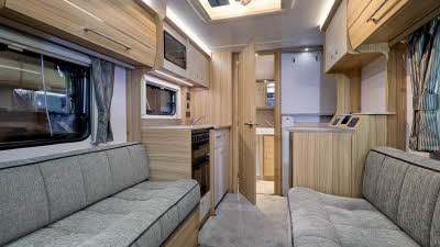 Bailey Phoenix GT75 420 has two grey sofas with a grey carpet.  The furniture is wooden and the rear interior door is open revealing the washroom