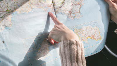 Woman in beige jumper pointing at location on a map