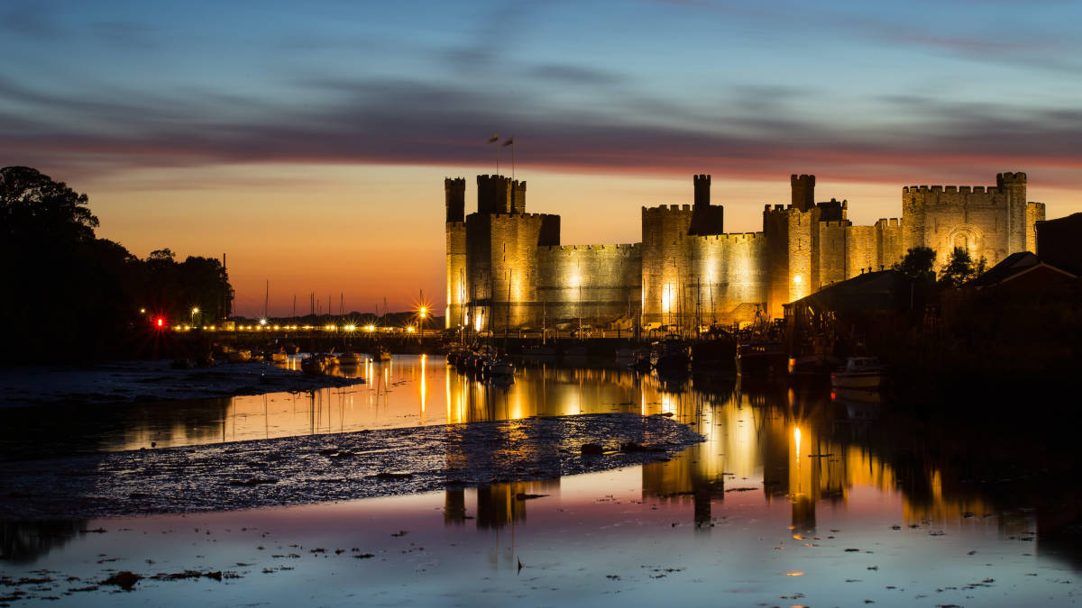Caernarfon Castle lit up at night. Reflection skimming off the water
