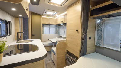 Interior of the Weinsberg CaraOne 390 QD with grey sofas, wood accents and a wooden floor.  The large roof light will let natural light flood in.  The French transverse fixed bed is at the front of the caravan.