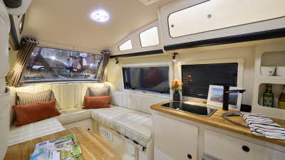 Barefoot Caravan Eclipse’s interior is cream with matching upholstery, there are four cushions on the sofa, two are stripy and two are orange.  There are wooden work surfaces.