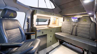 Wildtracks Campervans Explorer has a cream floor with black leather upholstery. The cabinets are green. The rising roof is open.