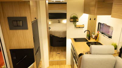 The Pilote P740FC Evidence has cream upholstery complemented with wood furniture.  The kitchen is to the right.  Through the wooden door there is a rear bedroom.