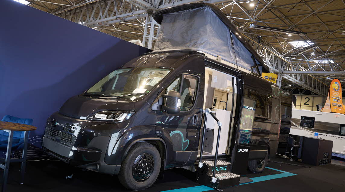 The Xplore CV X9 is black with turquoise decals.  There are two steps in front of the open sliding door which reveals the interior.  Its rising roof is fully extended.