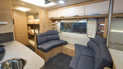 Knaus Südwind '60' 580 QS's interior has pale wood with dark blue upholstery.  The lounge seats face each other lengthways.  The kitchen basin can be seen at the front of the photograph.