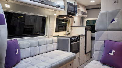 Auto-Sleeper Symbol has light grey embossed upholstery, with cream and grey overhead cabinets.  An oven, fridge and microwave is in the kitchen, with an flap to extend kitchen work surface.