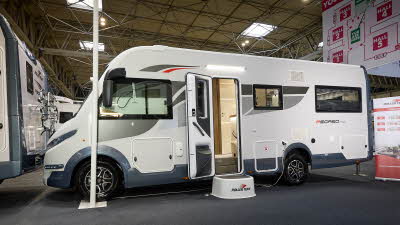 Roller Team Pegaso 745’s exterior has a white body with blue bumpers.  It has grey and red decals.  The habitation door is open and there is a large white step to gain easy access.