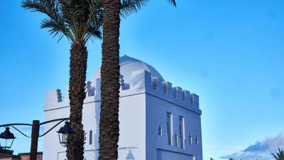 White mausoleum surrounded by clear blue sky and two palm trees in front