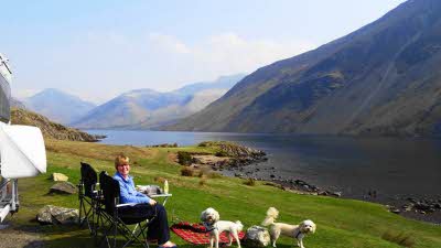 Woman sitting in camping chair by Wastwater in the Lake District with her two dogs and picnic blanket