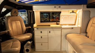 The Wildtracks Campervans Explorer has leather upholstery with cream cabinets.  The door to the top loading fridge is open.