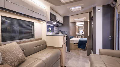 Swift Elegance Grande 780's interior has tan leather upholstery with pale cabinets.  The kitchen is placed in the centre with the bedroom just beyond.  There is a rear washroom and its door is open.