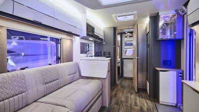 Swift Elegance Grande 850L’s interior has wooden units with cream doors.  It has beige upholstery which has embossed patterns.  The internal door is open revealing the washroom and to the rear, the bedroom