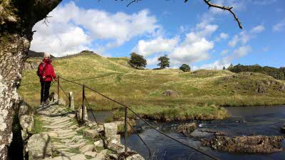 a walker stops to admire the view from an ancient stone bridge in the Lake District