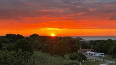An amazing sunset in a dark orange sky with a view of caravans and trees